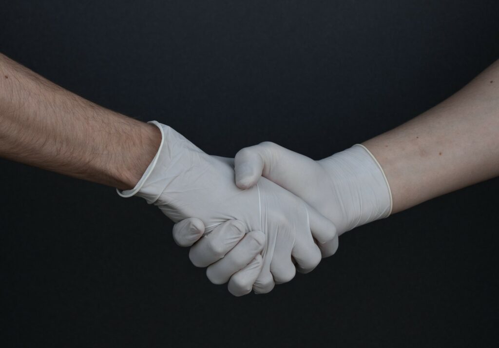 Zwei Personen mit Gummihandschuhen geben sich die Hand.