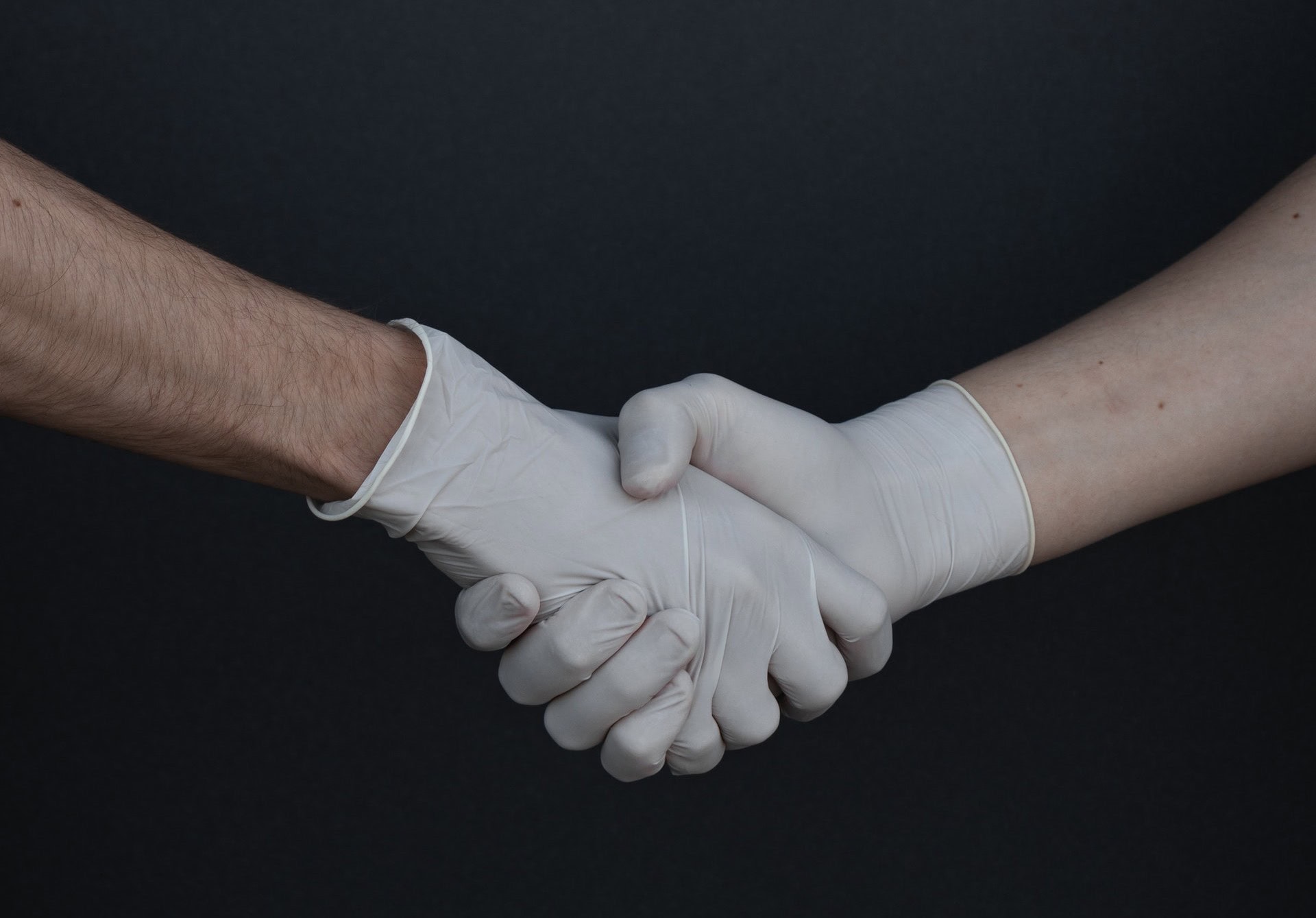 Zwei Personen mit Gummihandschuhen geben sich die Hand.